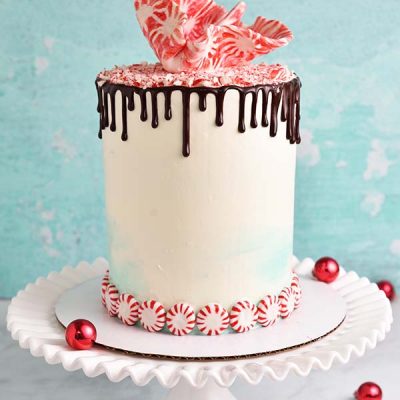 White and teal buttercream cake decorated with peppermint candies, cake sale and chocolate drips.