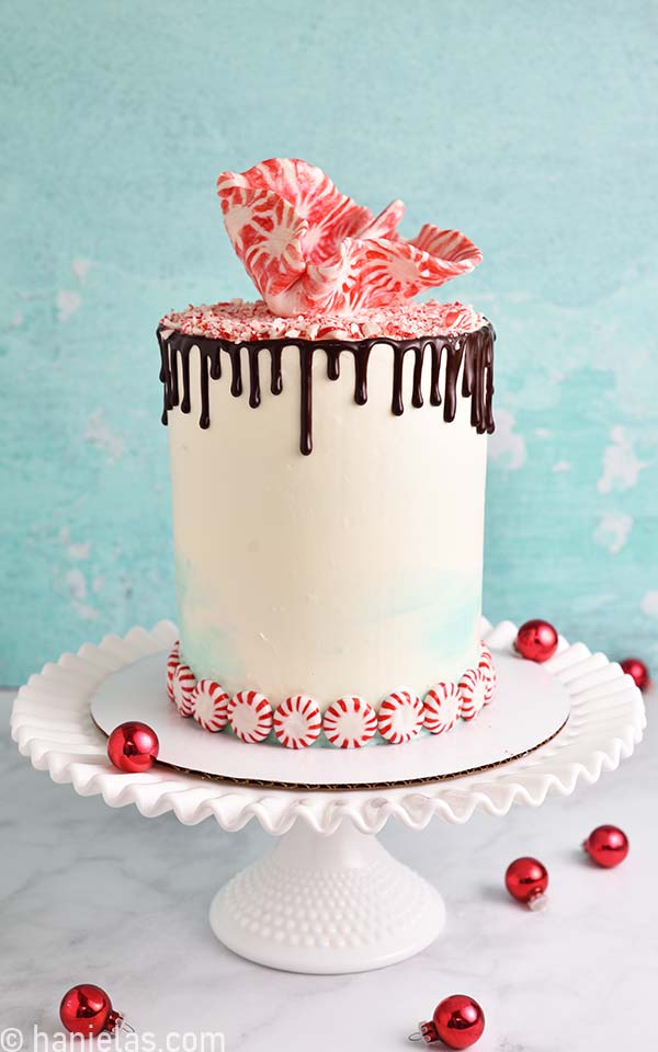 White and teal buttercream cake decorated with peppermint candies, cake sale and chocolate drips.
