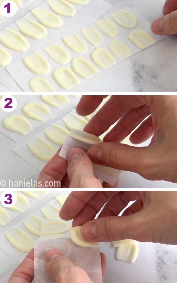 Fingers removing set chocolate petals from the parchment paper.