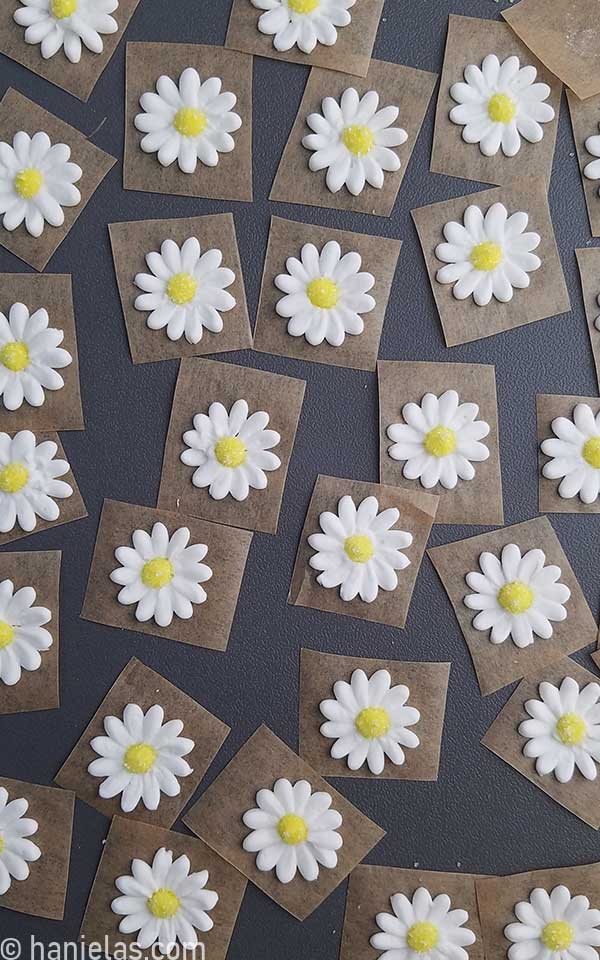 Piped royal icing flowers parchment squares, drying on a gray tray.