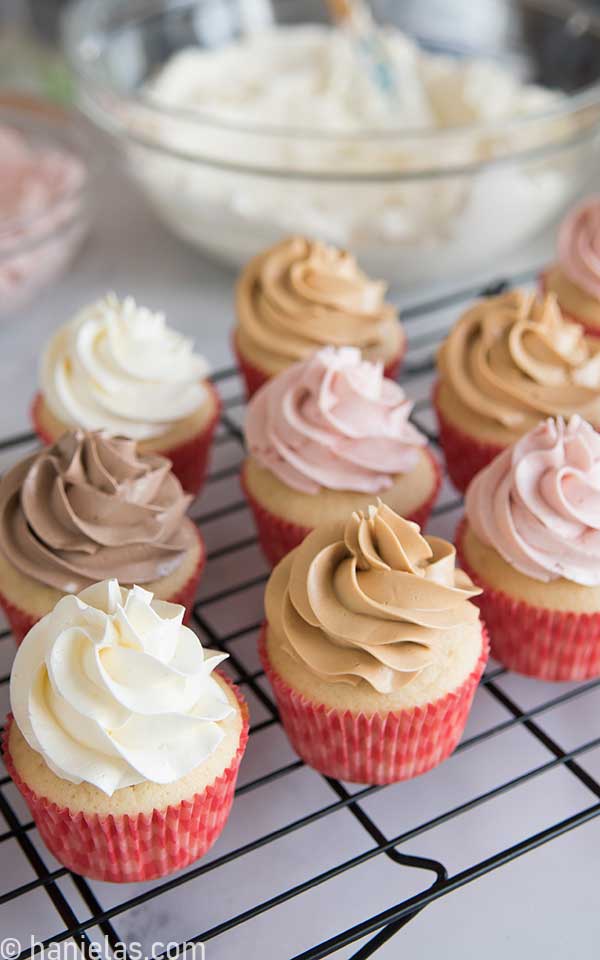 Cupcakes decorated with a buttercream swirl on a black cooling rack.