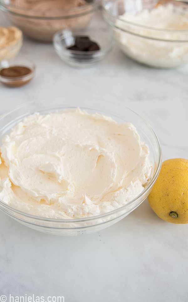 Lemon curd buttercream in a glass bowl with a yellow lemon on a side of the bowl.