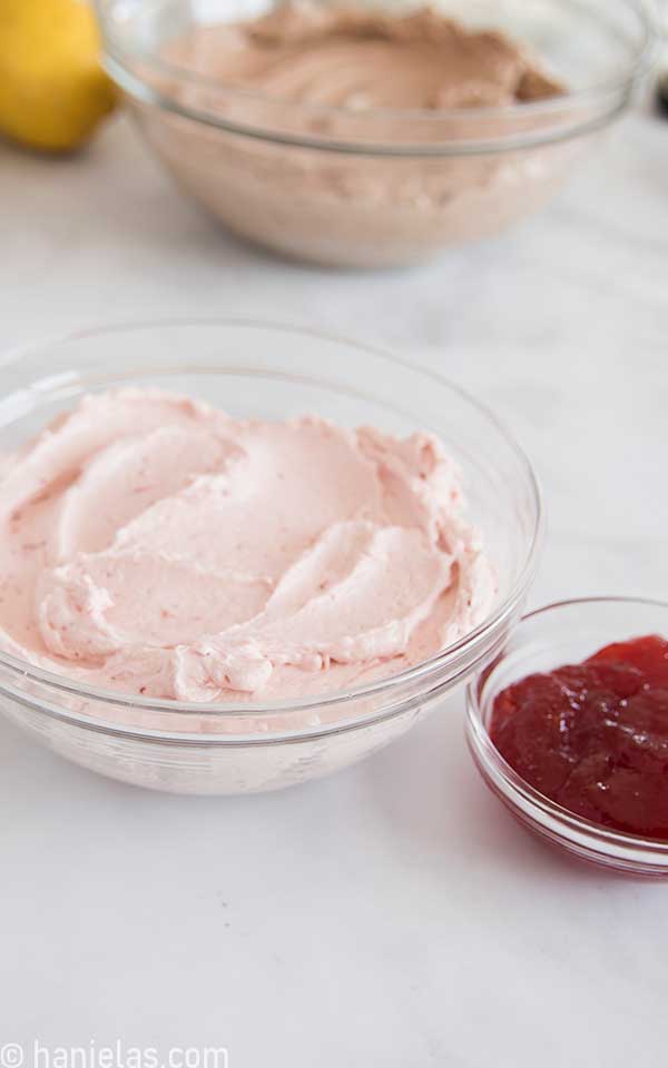 Strawberry buttercream in a glass bowl, with a small bowl of strawberry jam on the side.