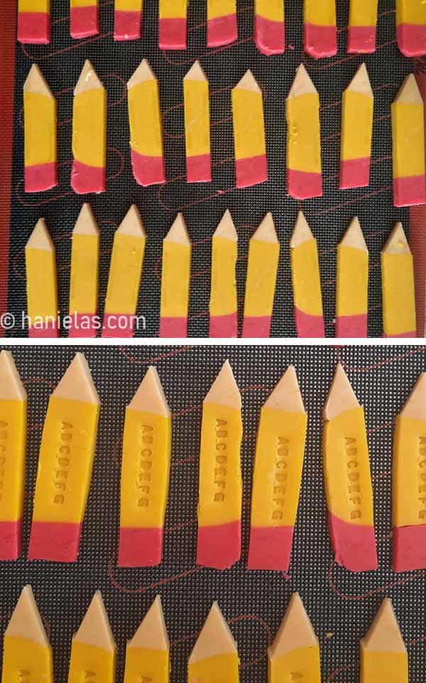 Pencil cookies on a baking sheet lined with black perforated mat.