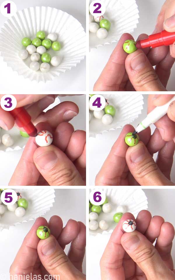Fingers holding sixlets candies, drawing on them with an edible marker.