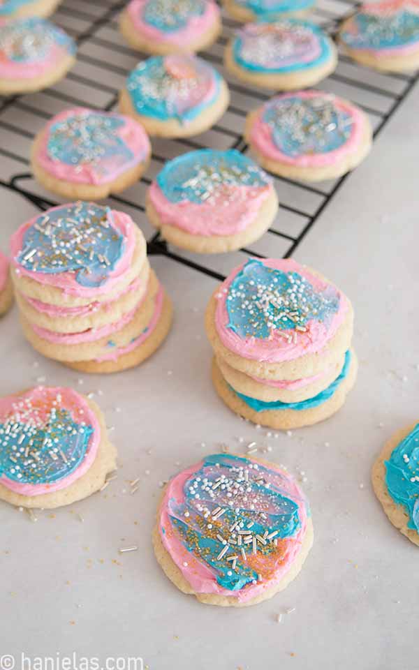 Round sugar cookies frosted with pink and blue frosting on a white parchment sheet.