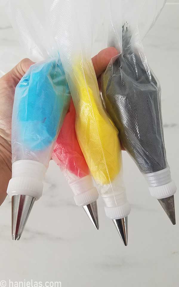Hand holding four piping bag filled with colorful buttercream.