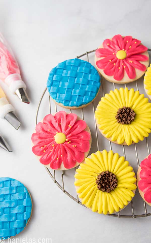 Round cookies decorated with buttercream displayed on a round cooling rack.