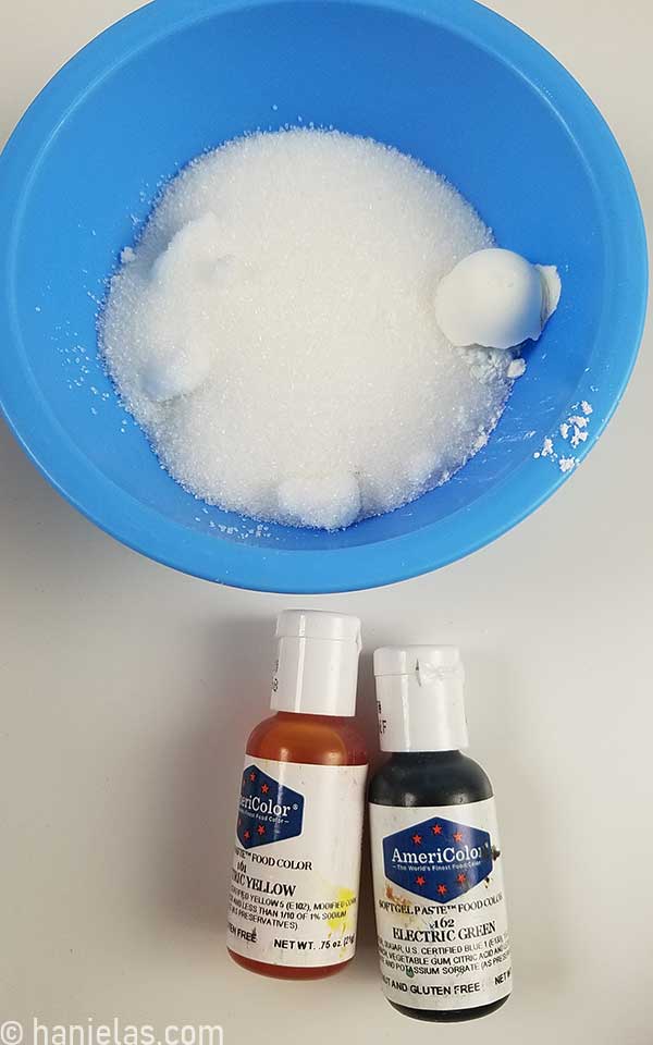 Blue bowl with granulated sugar and starch, two small bottle with gel food coloring.