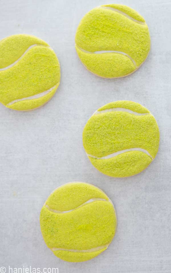Round decorated tennis ball cookies on a counter.