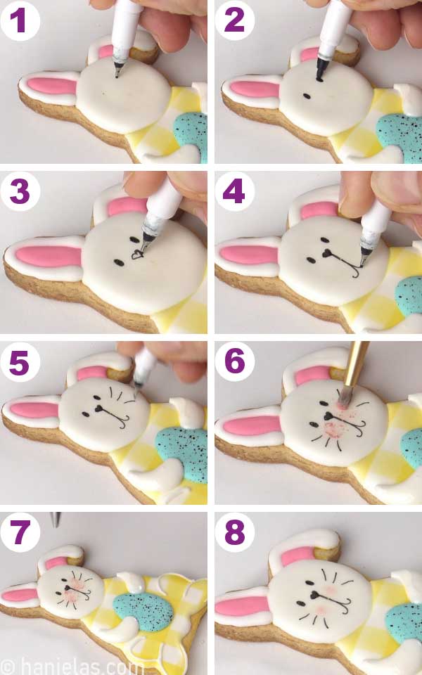 Hand holding a black edible marker drawing facial details onto a bunny cookie.