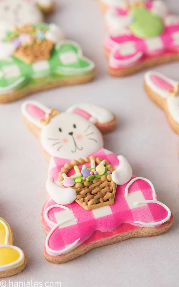 Sitting bunny decorated with royal icing, airbrushed with pink gingham pattern, holding royal icing easter basket.