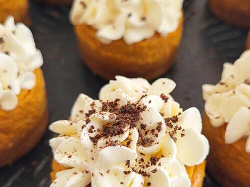 Detail of a small cake decorate with white whipped cream and chocolate bits, on a black plate.