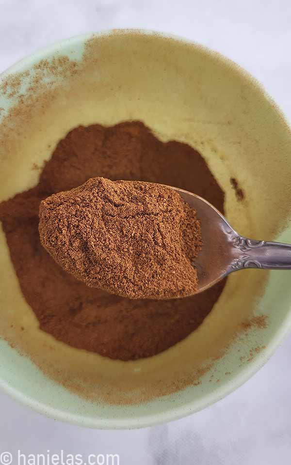 Spoon with a ground spice, above a small bowl.