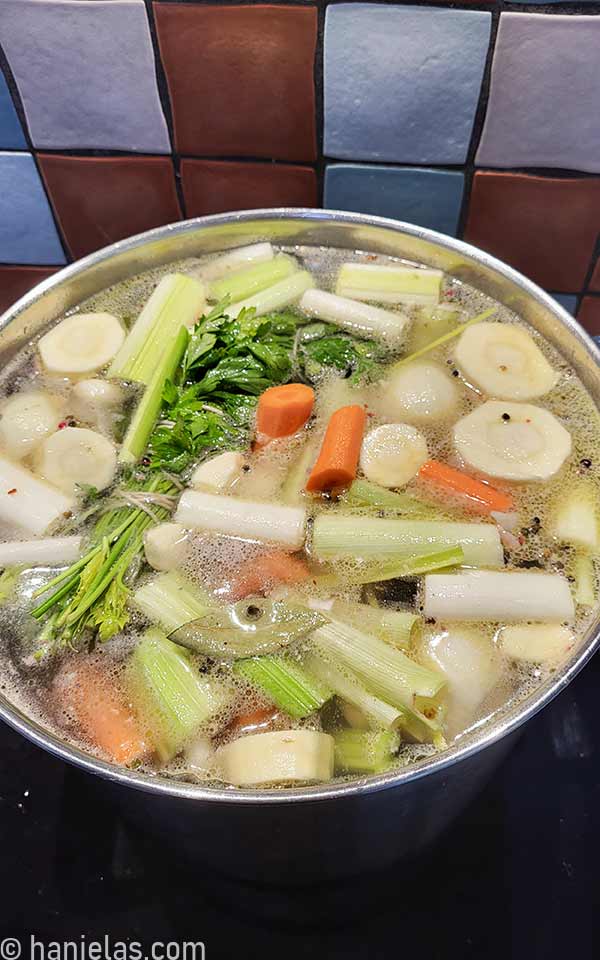 Large stainless steel pot with water and, fresh vegetables and meat.