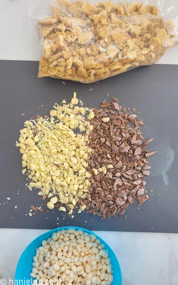 Ziploc bag filled with crushed cookies, chopped white and dark chocolate and marshmallows in a blue bowl.