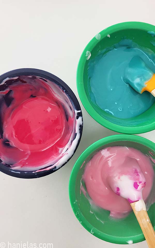 Three small bowls with colored icing.