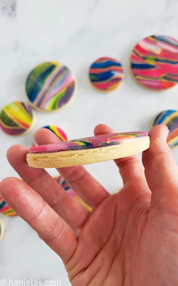 Hand holding a cookie decorated with icing showing the thickness of the icing.