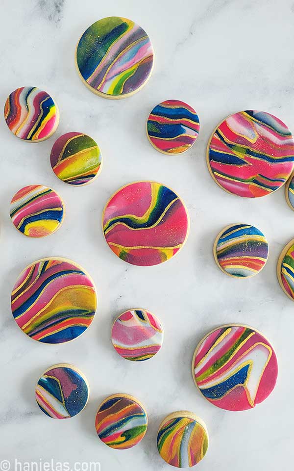 Round cookies decorated with colorful icing are displayed on a marble slab.