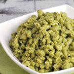 A white bowl full of green pasta.