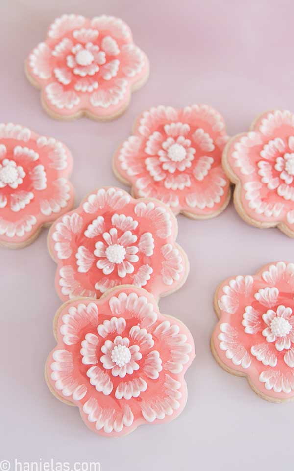 Several cookies decorated with royal icing displayed light pink background.