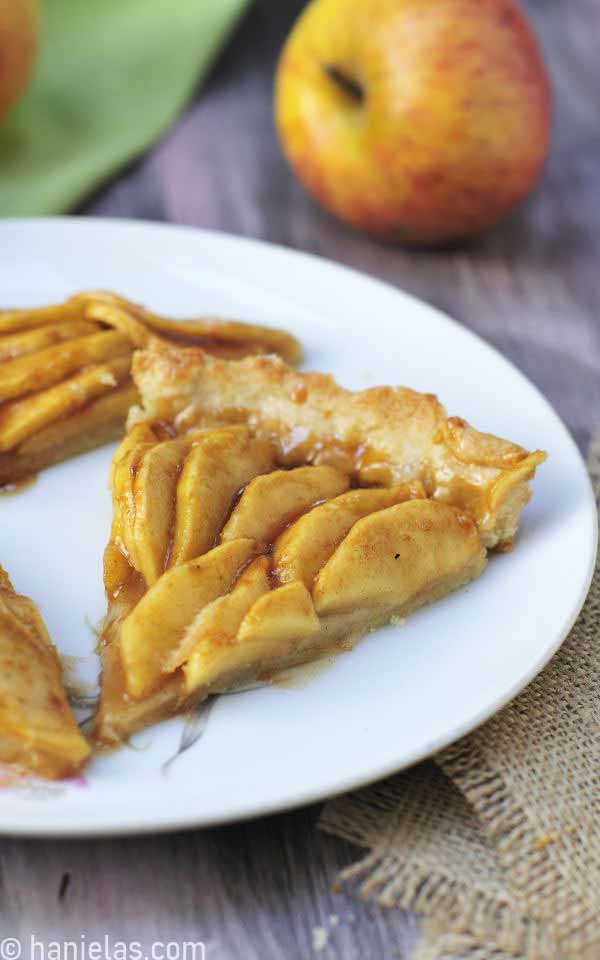 A close-up of an apple caramel tart slice served on a white plate.