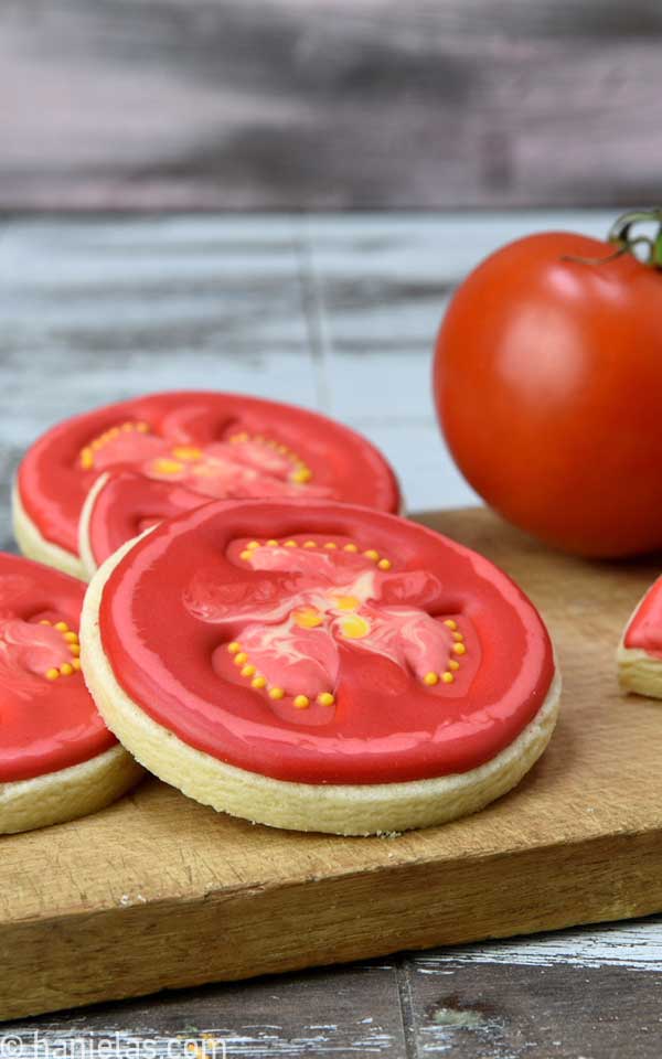 Royal icing decorated tomato cookies on a cutting board.
