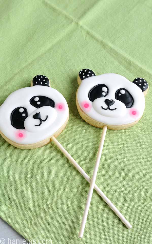 Two decorated cookies with a lollipop stick inside.