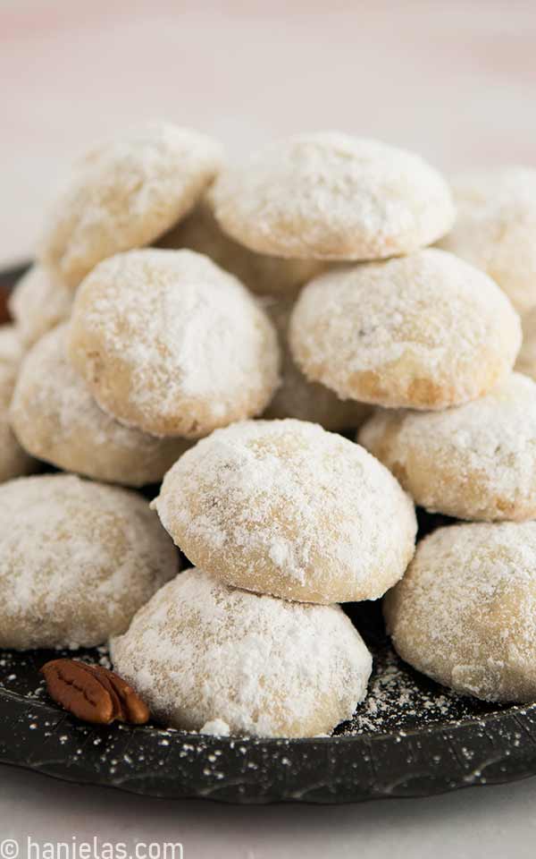 Cookies dusted with powdered sugar stacked on a black plate.