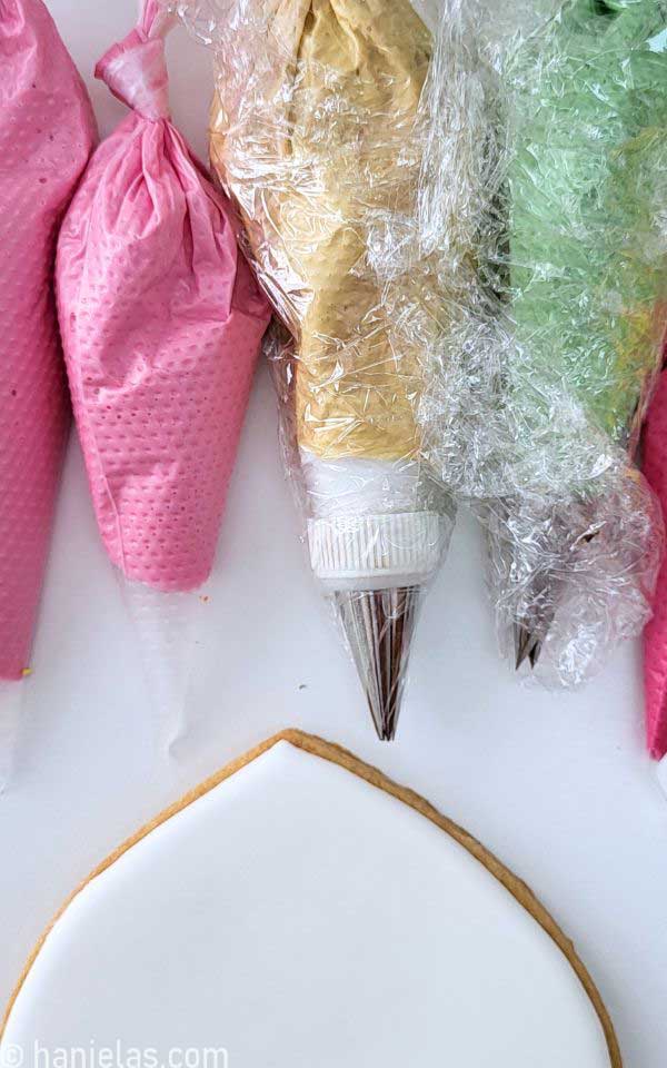 Cookie iced with white icing beside several piping bags with royal icing.