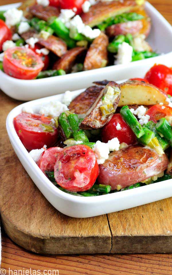 Roasted potatoes, asparagus, and tomatoes in a white dish.