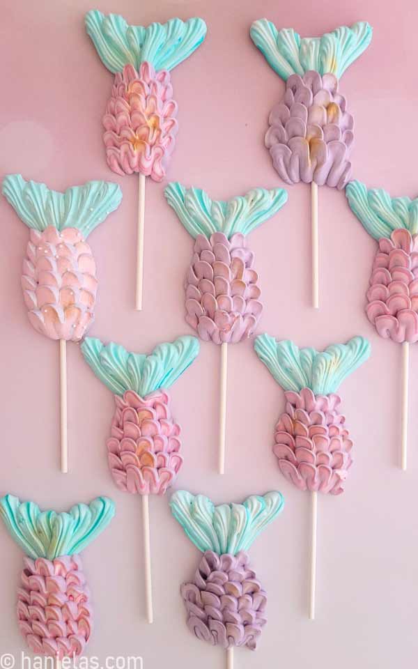 Pink, purple and teal meringue cookie pops on pink background.