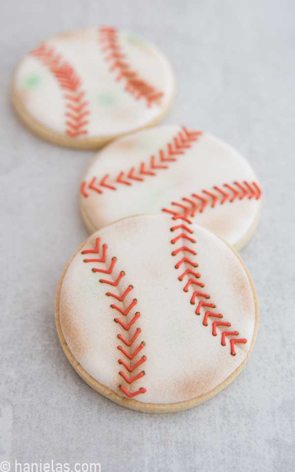 Three round cookies decorated with royal icing to look like baseballs.