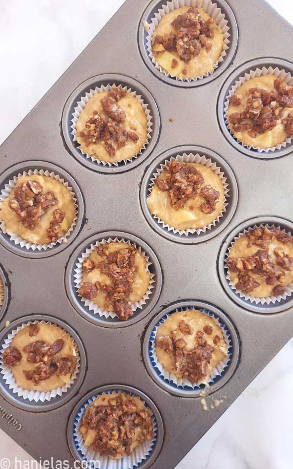 Muffin pan filled with batter and sprinkled with a nutty topping.