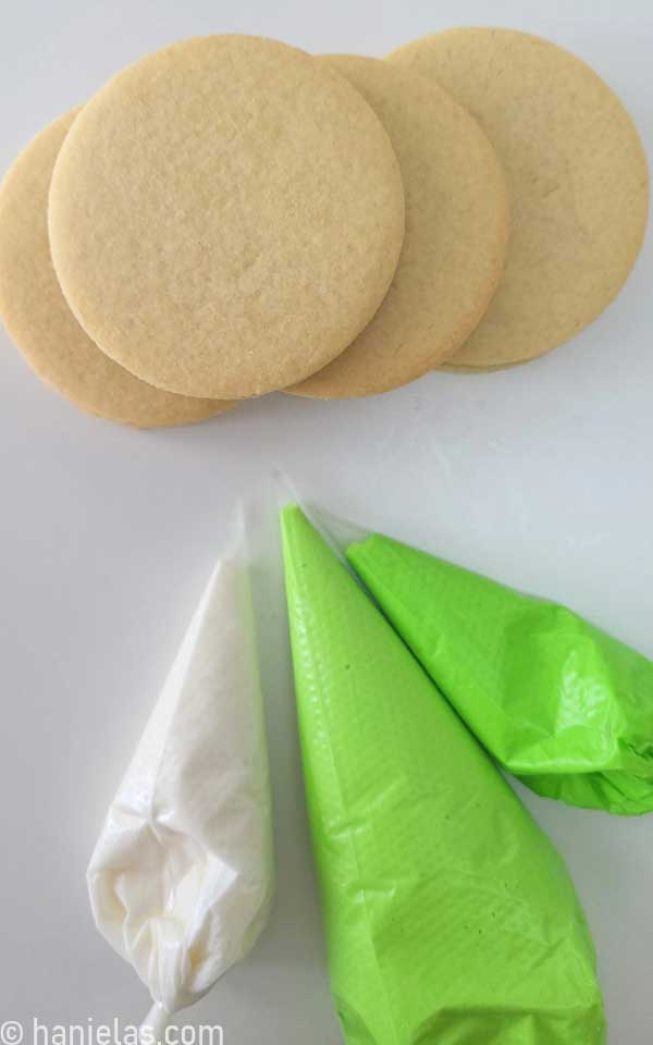 Round cookies and royal icing in piping bags.