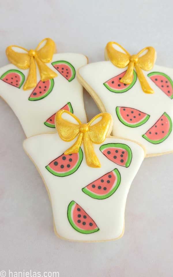 Cookies in a shape of a present decorated with a watermelon pattern and gold luster dust.