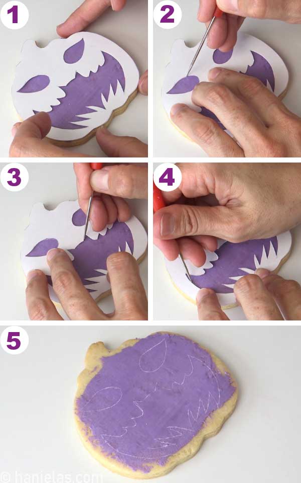 A cookie with a cardstock template on top, and a scribe tool tracing the outlines onto the icing.
