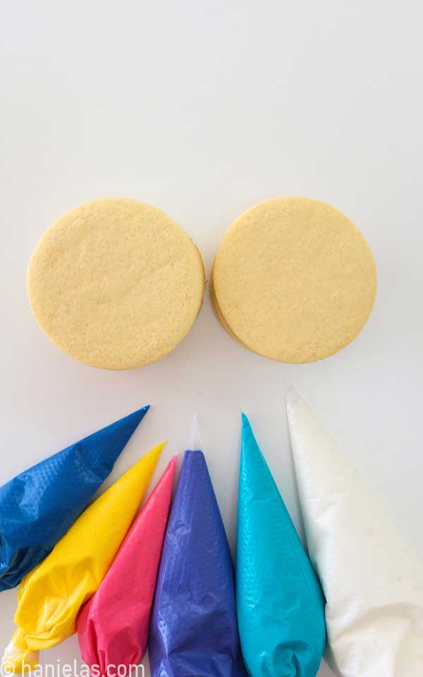 Round cookies and piping bags filled with royal icing.