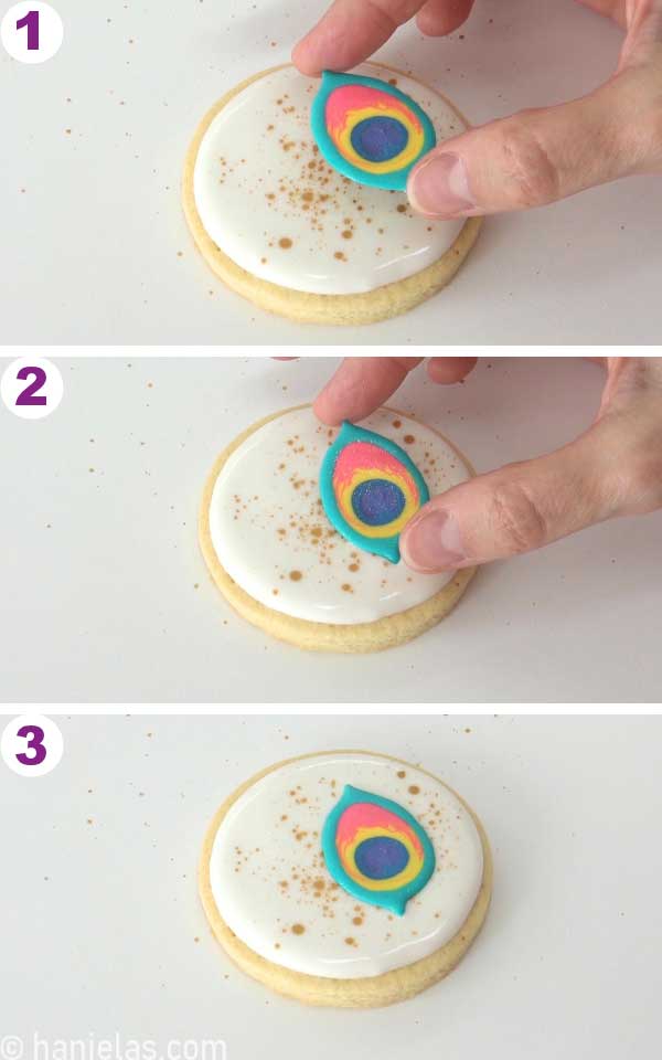 Hand holding a royal icing transfer, placing it onto a cookie iced with fresh royal icing.