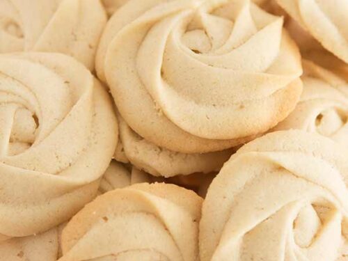 Cookies with lightly golden edges in a pink glass bowl.