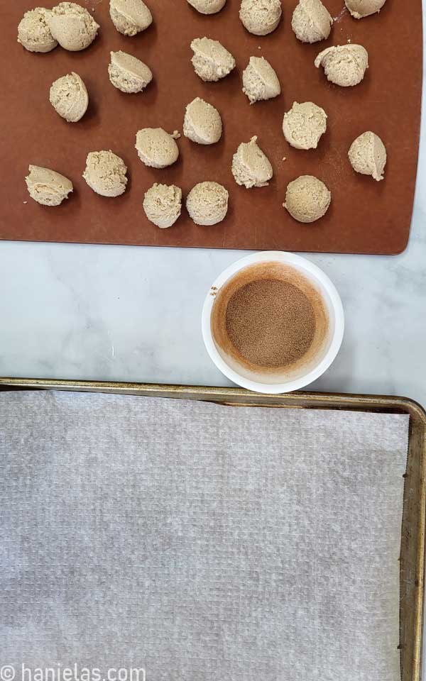 A small white bowl with cinnamon sugar next to a tray with cookie dough balls.