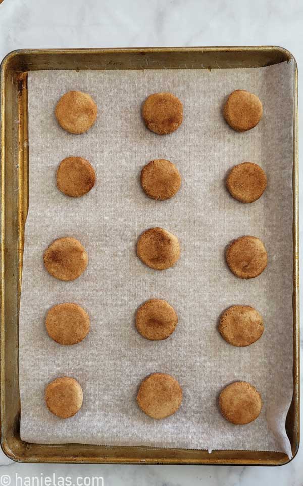 Baking sheet with flattened cookie dough balls rolled in cinnamon sugar.