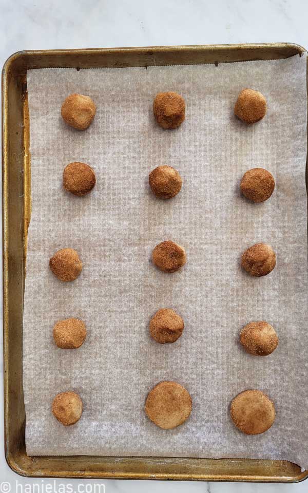 Baking sheet lined with parchment, with cookie dough balls, rolled in cinnamon sugar.