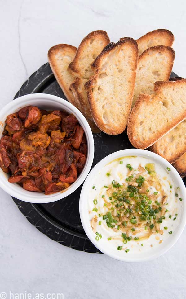 White serving bowls filled with roasted tomatoes, whipped feta and toasted bread slices.