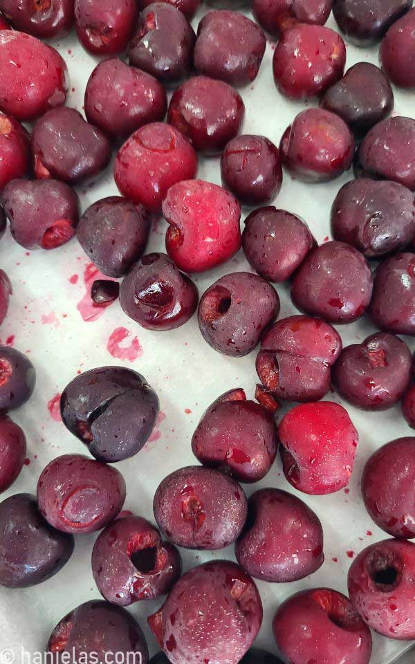 A close-up of frozen cherries on a baking sheet lined with parchment.