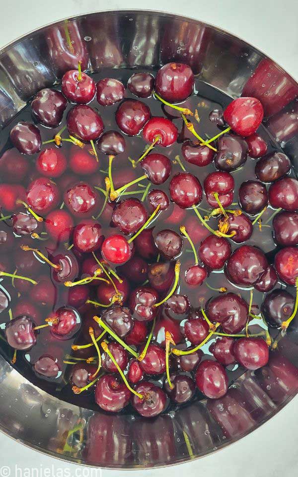 Cherries in a stainless steel bowl in water.