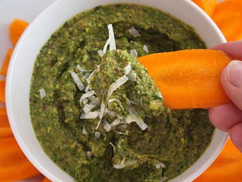 Fingers holding a piece of sliced carrot with a green dip on the carrot.
