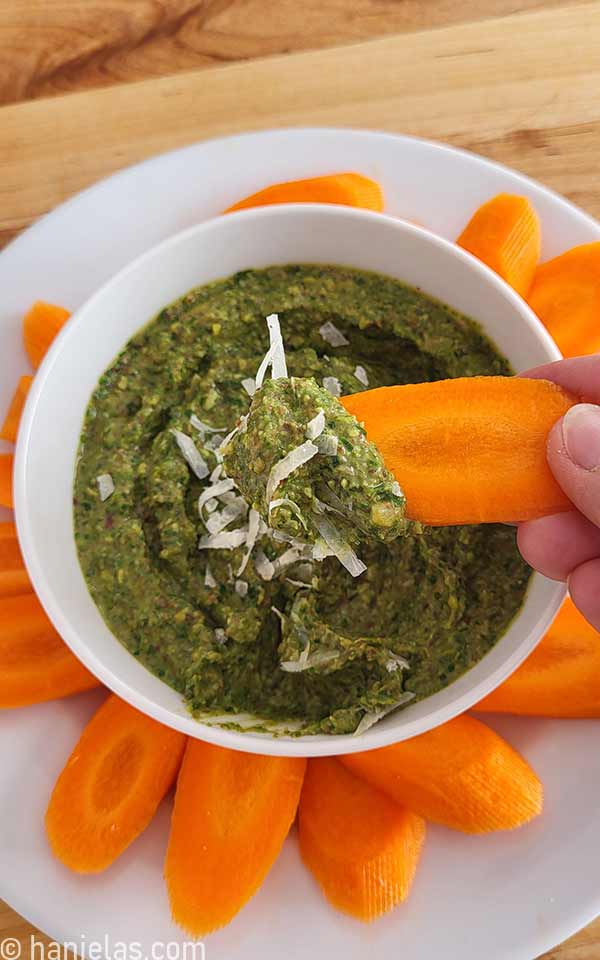 Fingers holding a piece of sliced carrot with a green dip on the carrot.