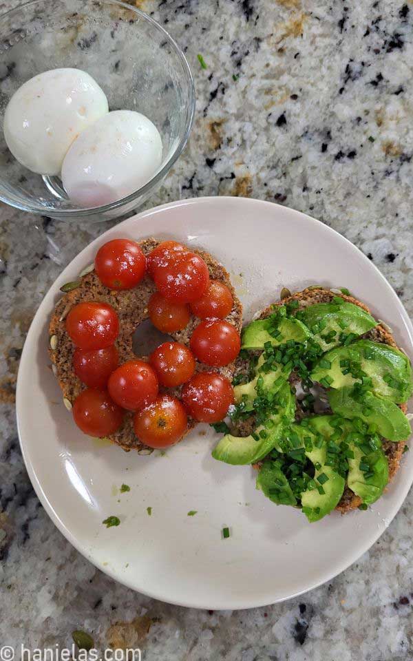 Sliced bagel topped with sliced cherry tomatoes, avocado and chives.