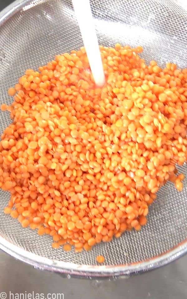 Legumes in a sieve, water running through them.